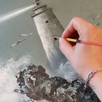 a person is painting a lighthouse on a canvas
